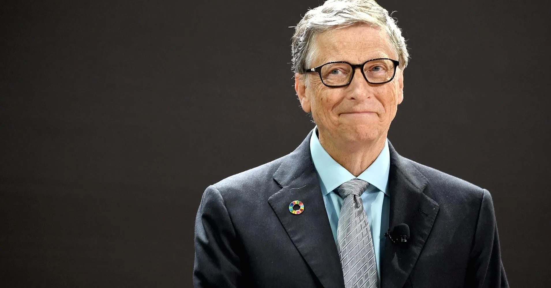 Bill Gates in glasses and a suit, smiling, on black