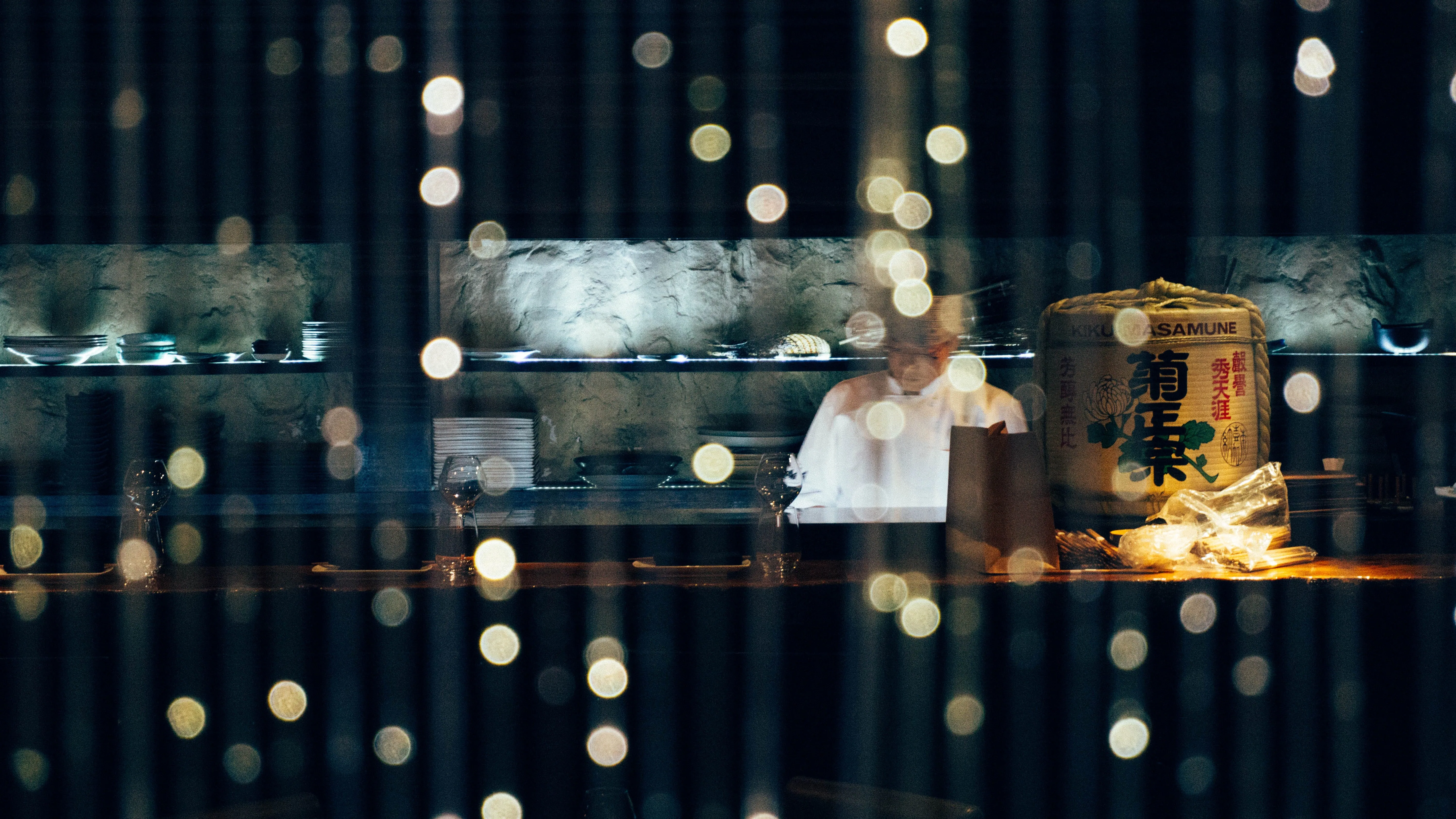 A chef at work in a dimly lit Japanese restaurant kitchen, seen through bokeh lights