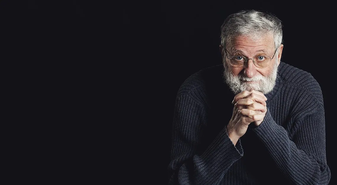 Don Norman, a portrait with his hands clasped, on black