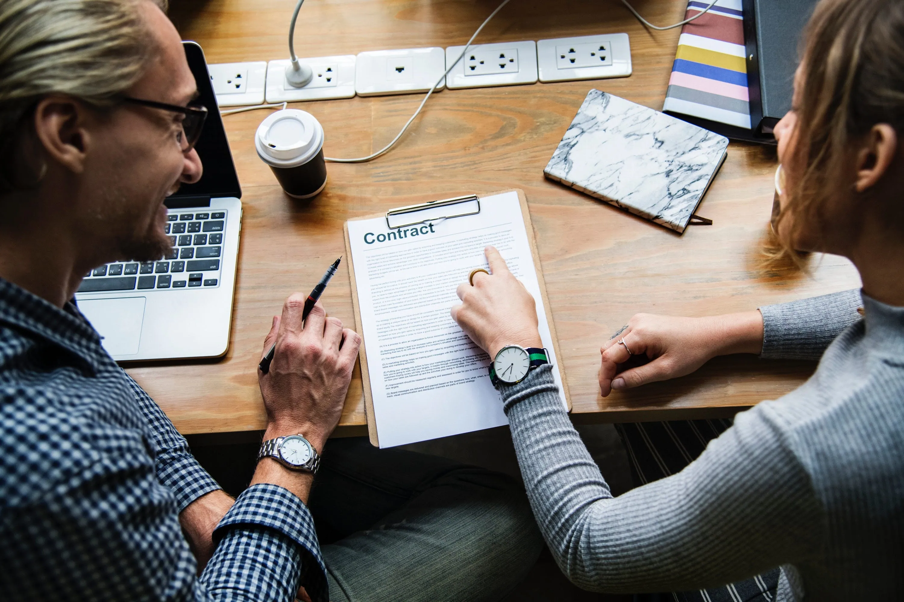 Two people smiling over a clipboard with a document titled “Contract” on a wooden desk