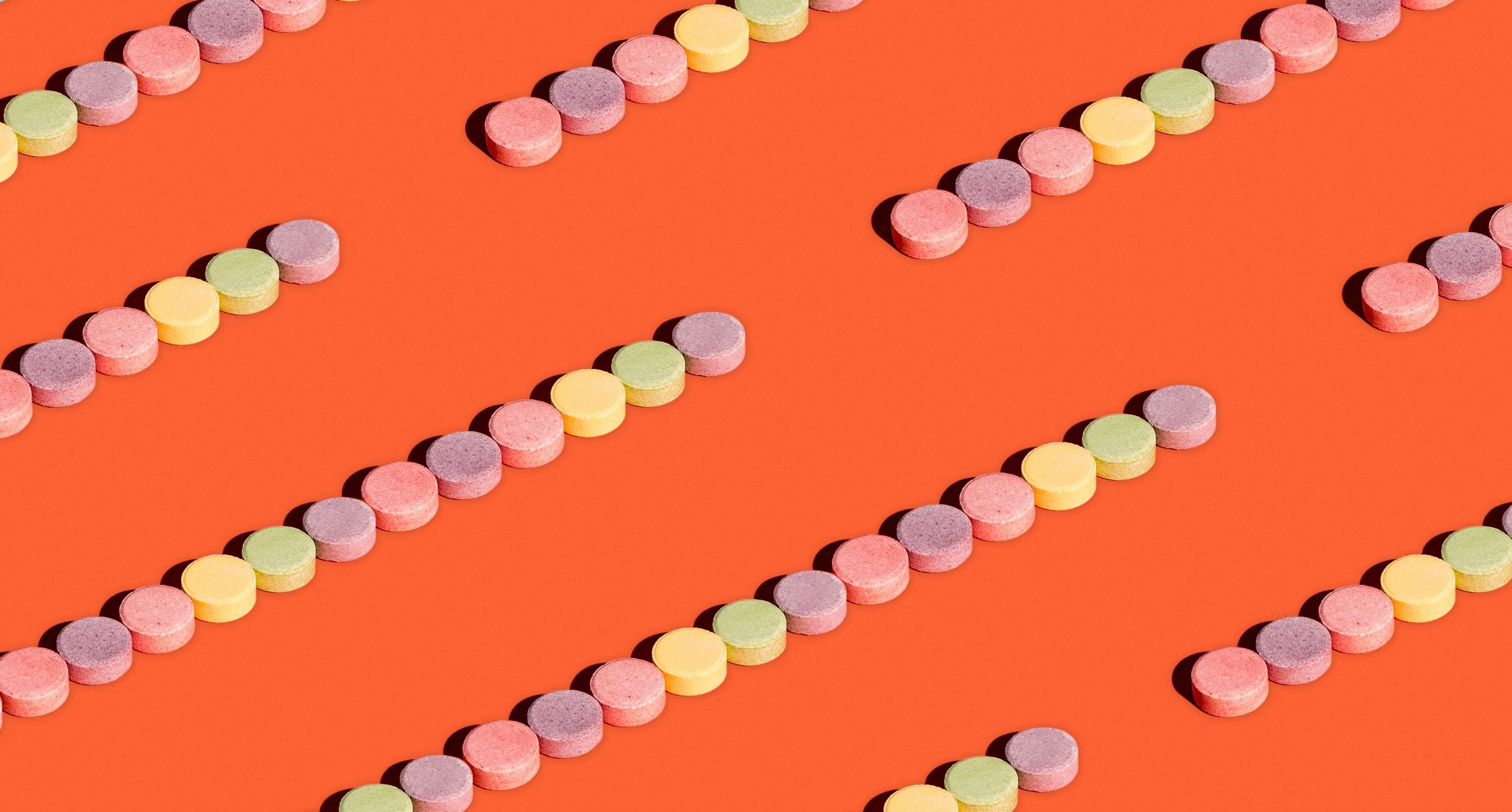 Diagonal rows of pastel pink, purple, yellow and green candy tablets on orange