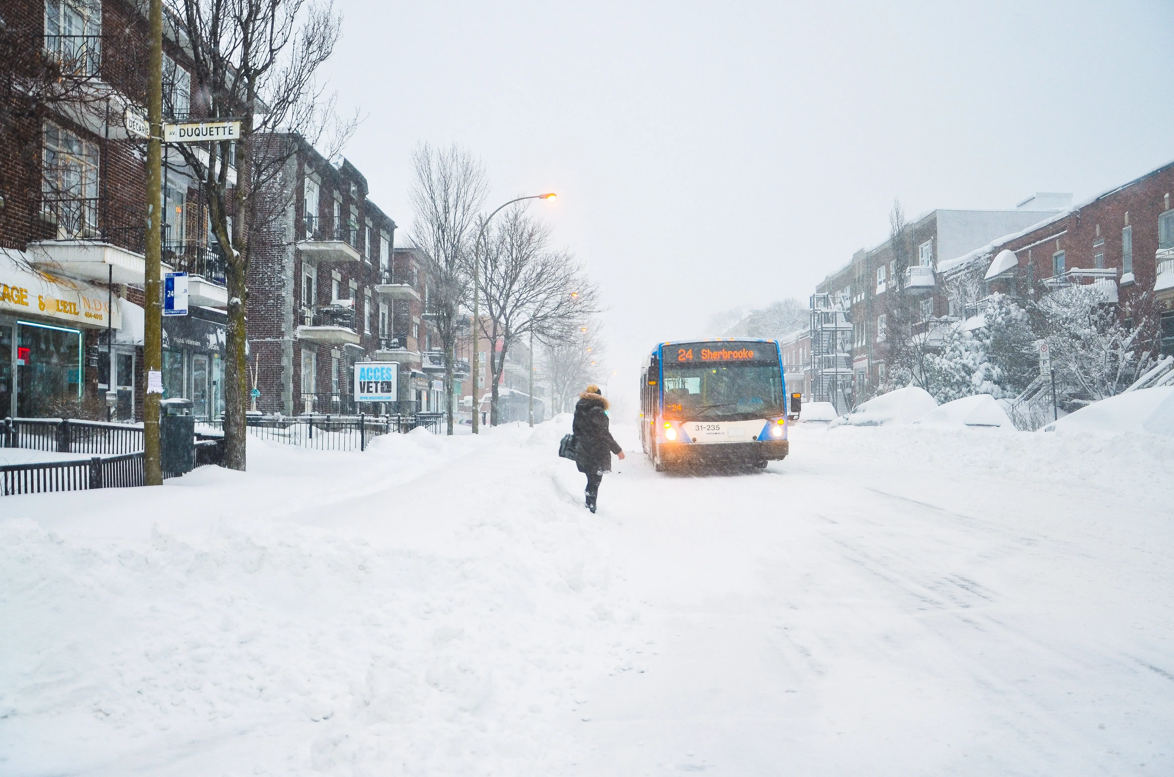 A person walking through a snow-covered street towards a bus
