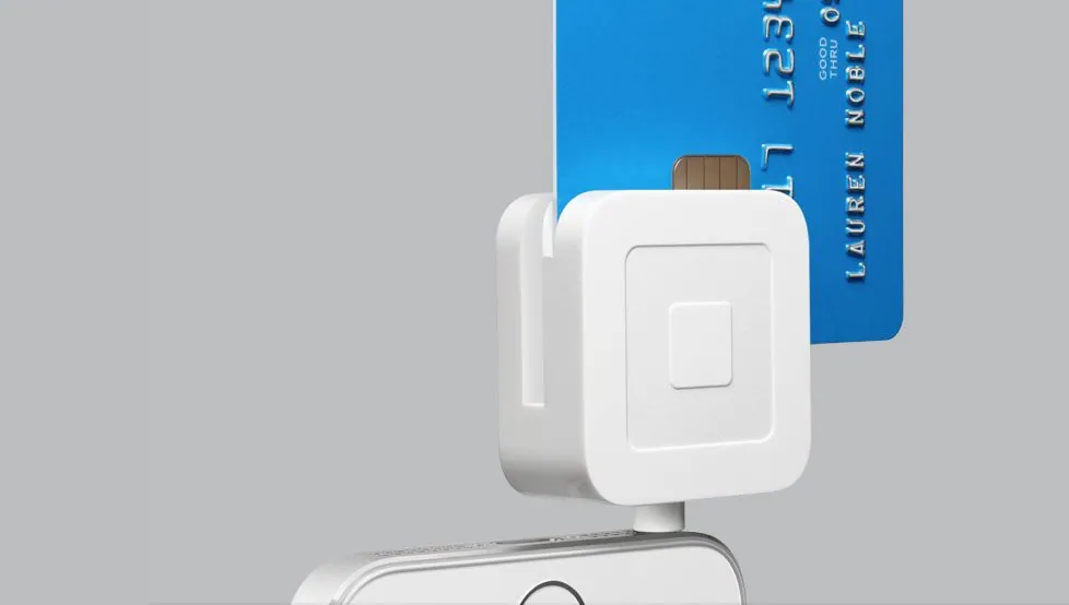 A Square card reader attached to a phone, with a blue credit card inserted