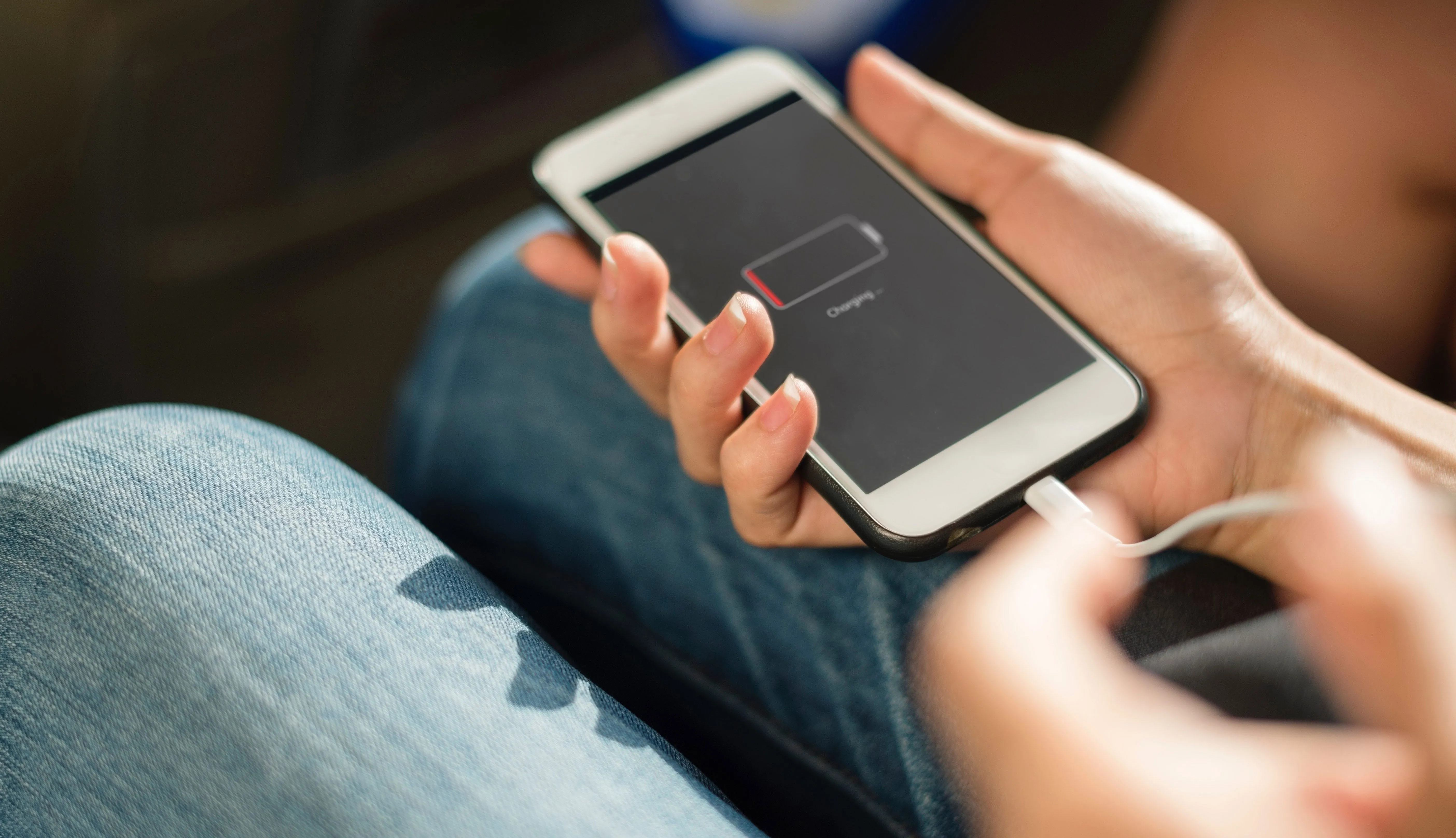 Hands holding a phone with an empty battery, plugged in to charge